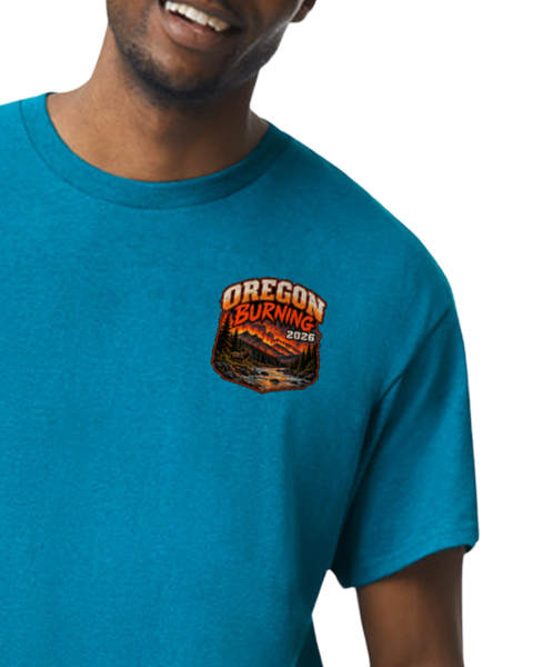 A close-up of a man wearing a heathered teal blue t-shirt with a 'Oregon Burning 2026' graphic printed on the left chest.