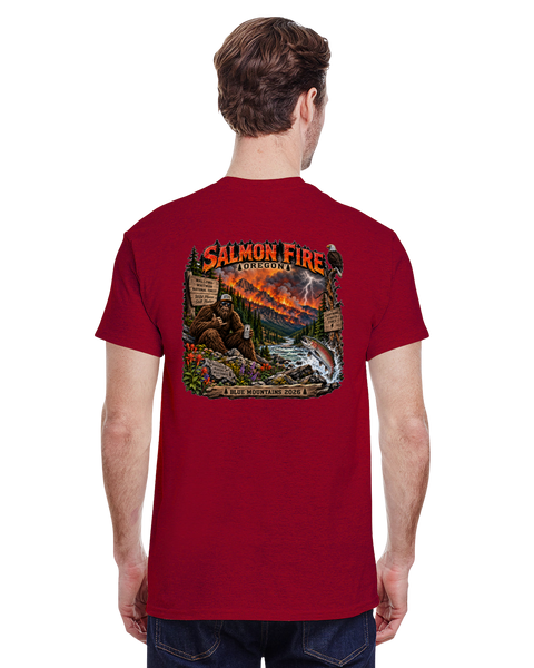 A man viewed from behind wearing a red t-shirt with a large, detailed back graphic depicting a salmon jumping, wildfire in a forest, a Sasquatch with a beer, and a river and the text 'SALMON FIRE 2026'.