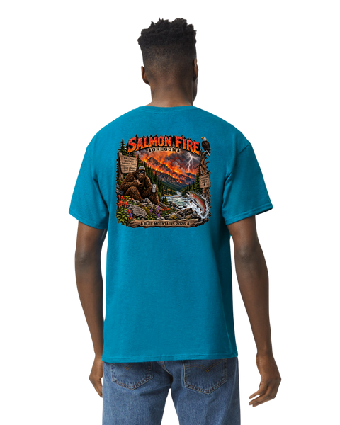 A man viewed from the back wearing a bright turquoise blue t-shirt with a large graphic print on the back. The graphic features a wild fire scene with a bigfoot, lightning, and the text 'SALMON FIRE' and 'BLUE MOUNTAINS 2026'.